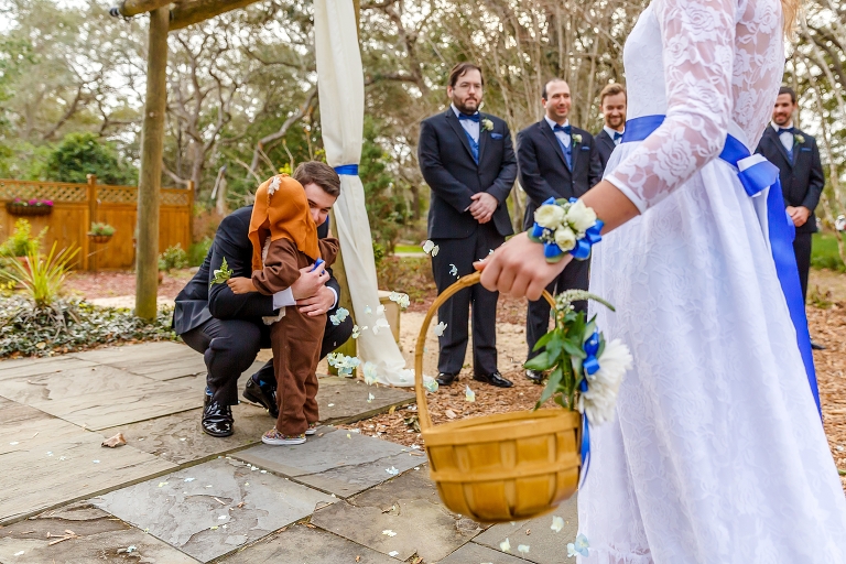 the groom hugs their ring bearer in his Ewok costume at their DIY garden wedding ceremony