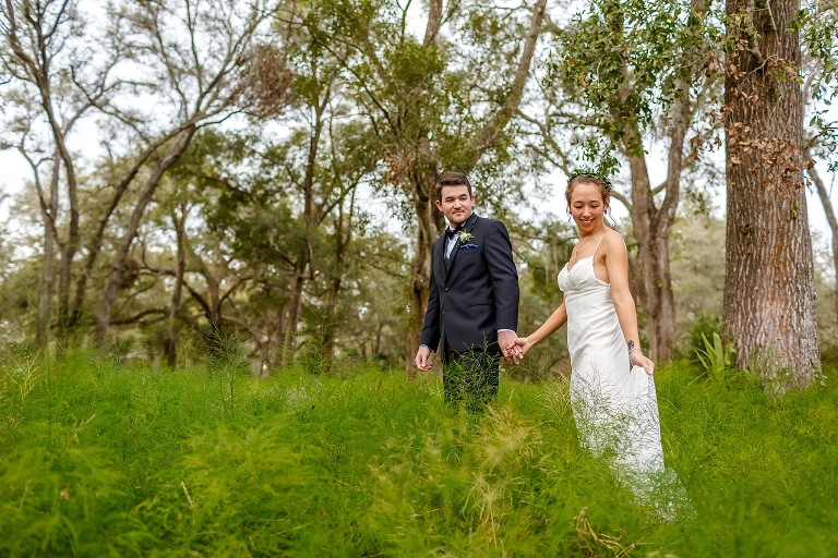 the groom leads his bride through the brush after their DIY garden wedding at Harmony Gardens