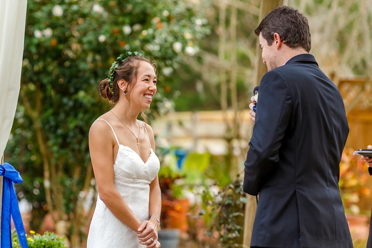 the bride laughs as her groom shares his vows with her during their DIY garden wedding ceremony
