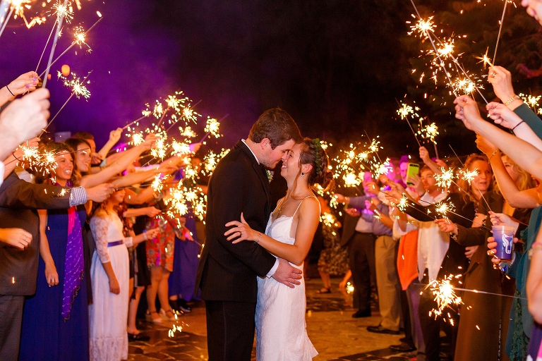 the bride & groom laugh as they walk through their guests holding sparklers
