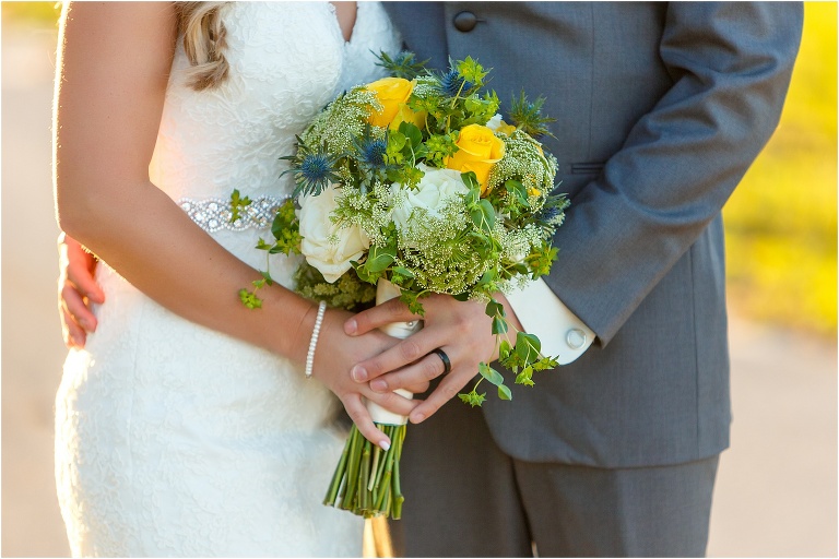 closeup of the yellow, white, & blue bridal bouquet being held by the bride & groom