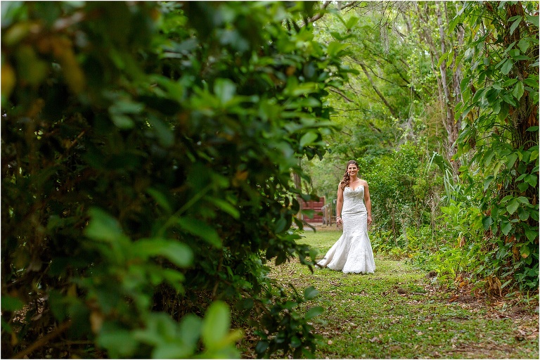 the bride smiles as she approaches her soon-to-be husband among the greenery at their Bakers Ranch wedding