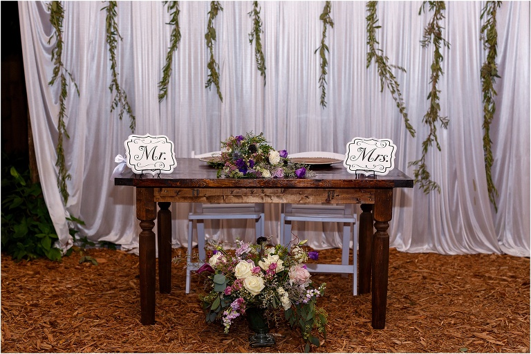 sweetheart table with purple and pink accented floral bouquets designed by Bliss Flower and Design Studio