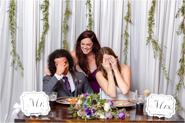the bride and groom giggle embarrassingly as the groom's sister laughs behind them