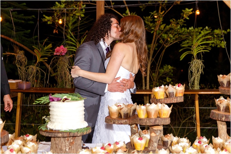 bride & groom kiss behind their dessert table at Harmony Gardens wedding venue