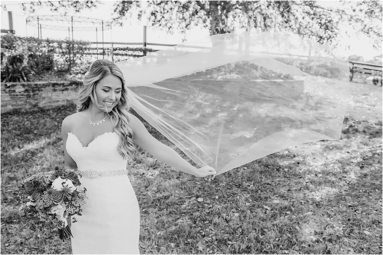 the bride's veil flies behind her in the wind as she prepares for her Cottom Farm wedding ceremony