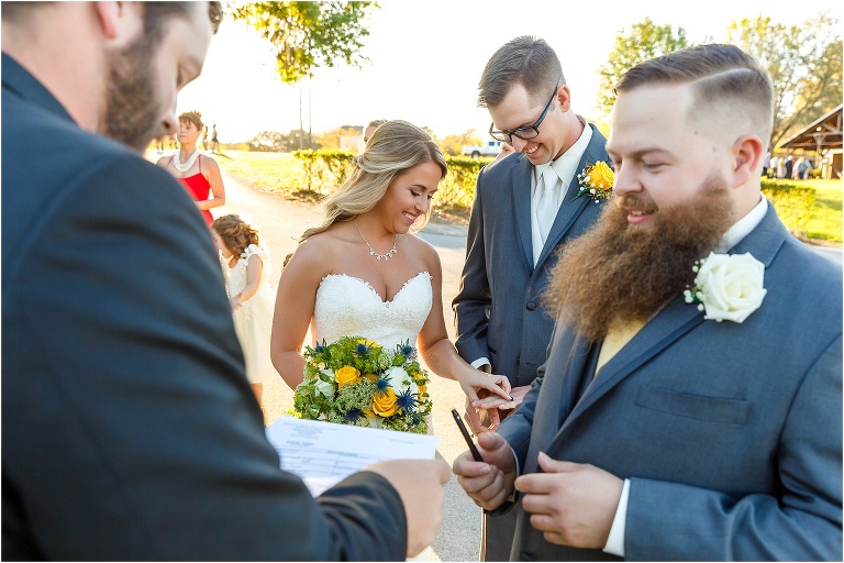 the bride admires the groom's wedding ring as the best man prepares to sign their marriage license