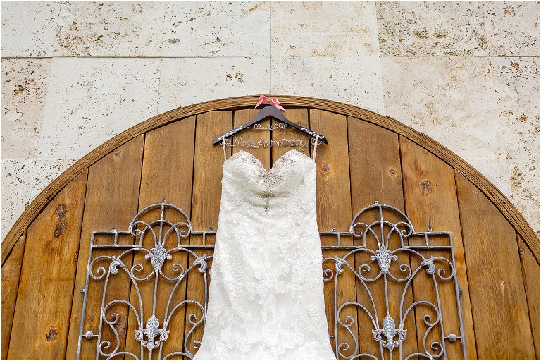 the bride's wedding dress hands on a personalized hanger in front of the ornate wooden doors at their Bakers Ranch wedding