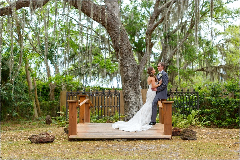the bride leans against her groom on the bridge under the massive oak tree