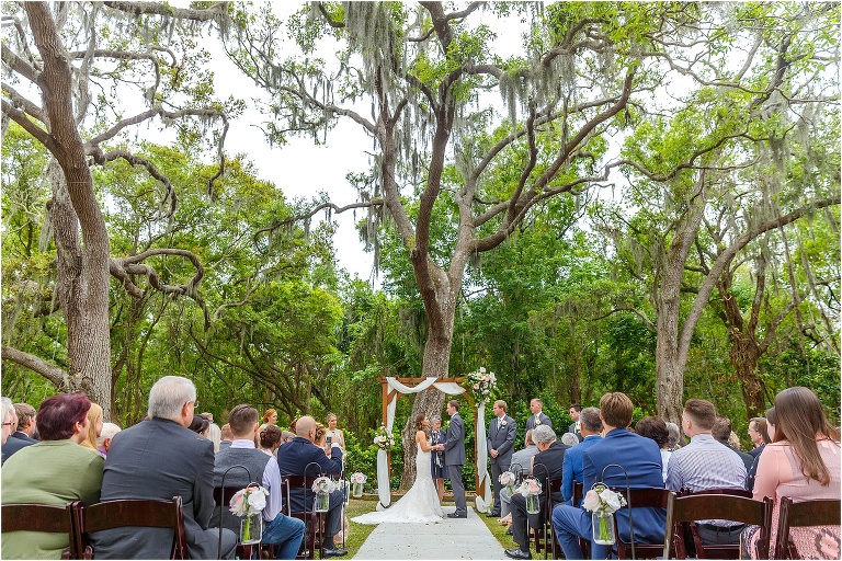 the bride & groom exchange vows under a large oak tree surrounded by their friends & family during their Bakers Ranch wedding ceremony