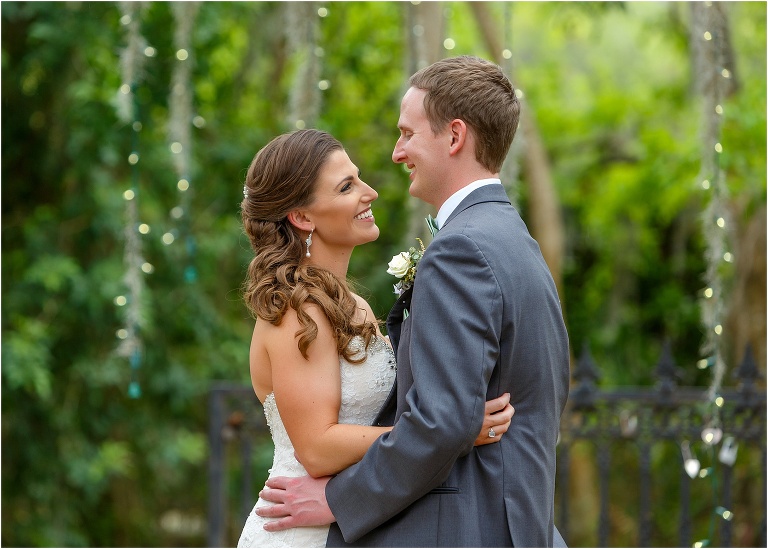 the bride and groom laugh together as the twinkle lights glow behind them