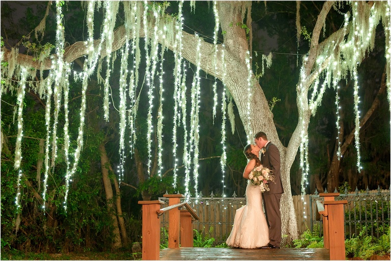the bride and groom kiss under the twinkle lights at night