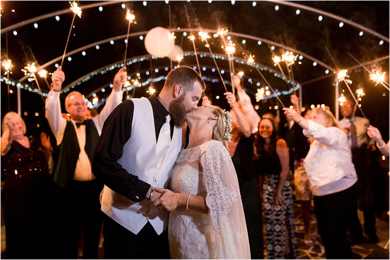 the bride & groom kiss under the light from their guests' sparklers at their Harmony Gardens wedding reception