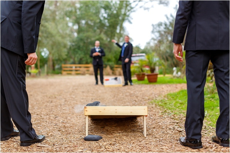the groom & his groomsmen relax with a game of corn hole before the Harmony Gardens wedding ceremony