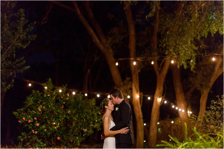 groom kisses bride's forehead at night under the market lights among the trees
