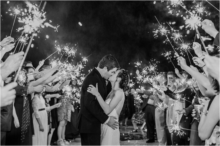 bride & groom kiss surrounded by the sparklers their guests are holding during their grand exit