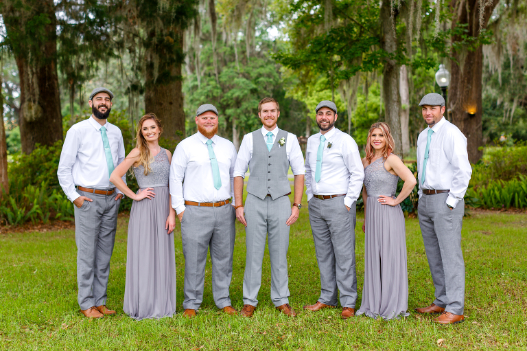 the groom surrounded by his grooms-people in grey outfits with teal accents