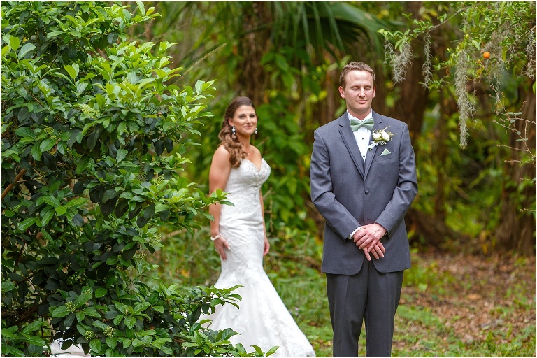 the groom keeps his eyes closed as his bride approaches behind him for their first look among the trees