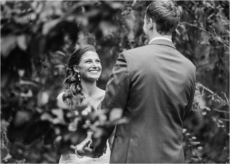 the bride beams as her groom turns around to see her during their first look on their wedding day