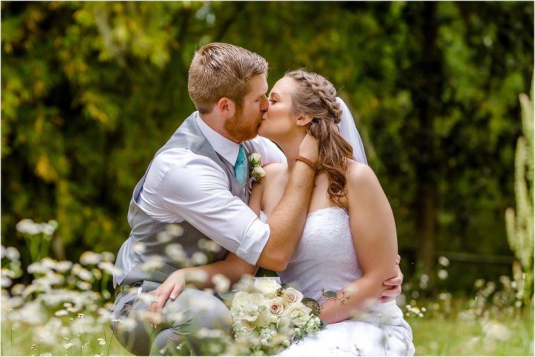 the groom kisses his bride among the wildflowers