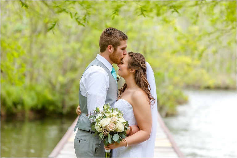 the groom kisses his bride's forehead at the end of the dock before their Bellemoor Plantation wedding
