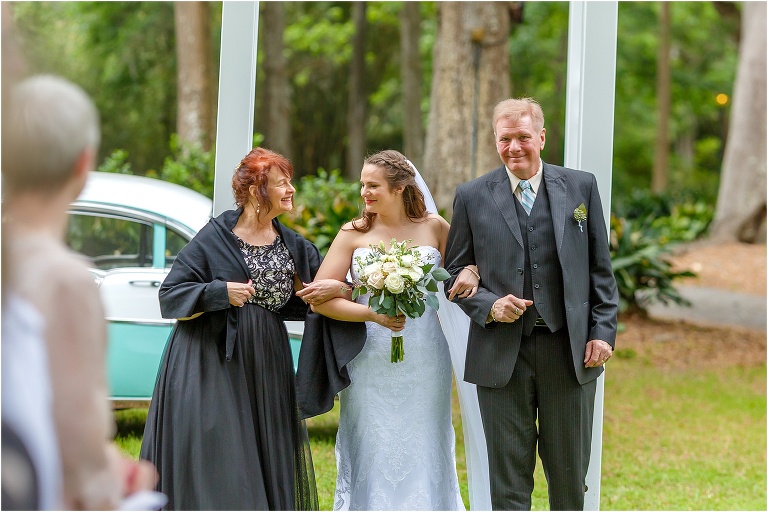 the mother of the bride smiles at her daughter as they walk down the aisle at their Bellemoor Plantation wedding ceremony