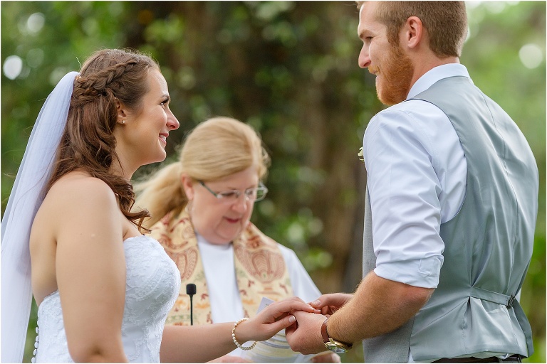 the bride and groom smile at each other as the groom places the bride's ring on her finger