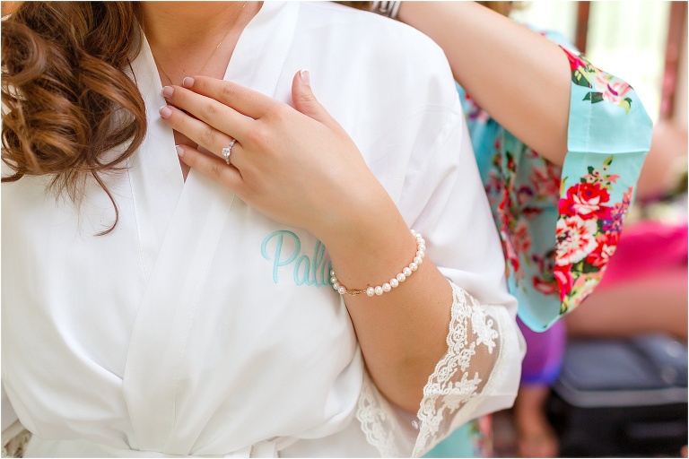 the bride touches her necklace as her bridesmaid finishes putting it on her