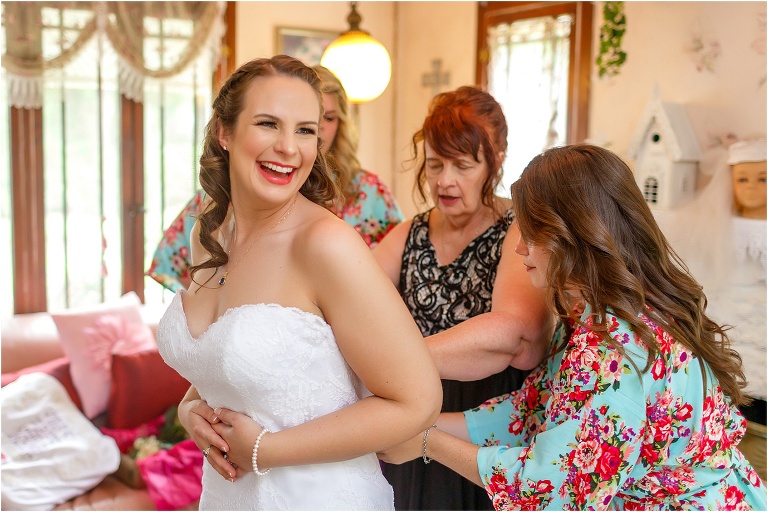 the bride laughs as her mother and two bridesmaids help fasten her dress before her Bellemoor Plantation wedding