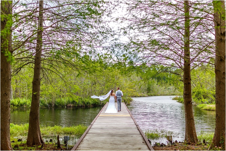 the bride and groom walk hand in hand down the dock at their Bellemoor Plantation wedding as her veil blows in the wind