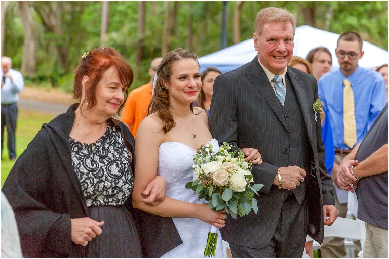 the bride has tears in her eyes as her parents walk her down the aisle