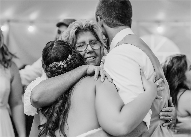 the bride and groom share a group hug with the groom's mother