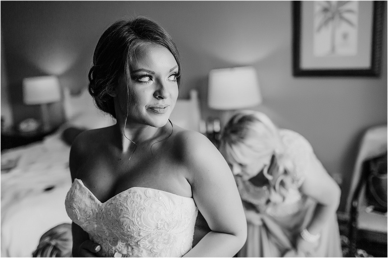 the bride looks out the window as her mother buttons her dress before her crystal river wedding