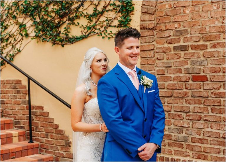 bride sneaks up behind grinning groom for first look before wedding ceremony