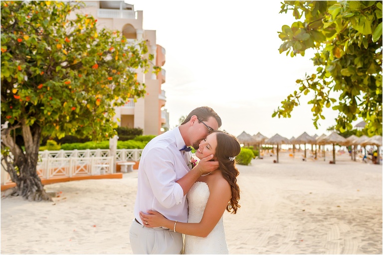 the groom kisses his bride's cheek as she smiles between two fruit trees after their Montego Bay wedding