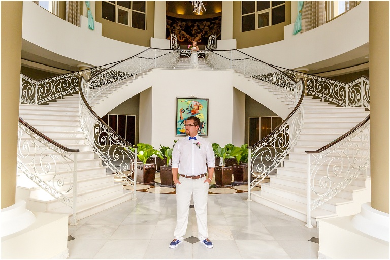 the groom awaits his bride between two grand staircases in the Iberostar Rose Hall Suites hotel lobby