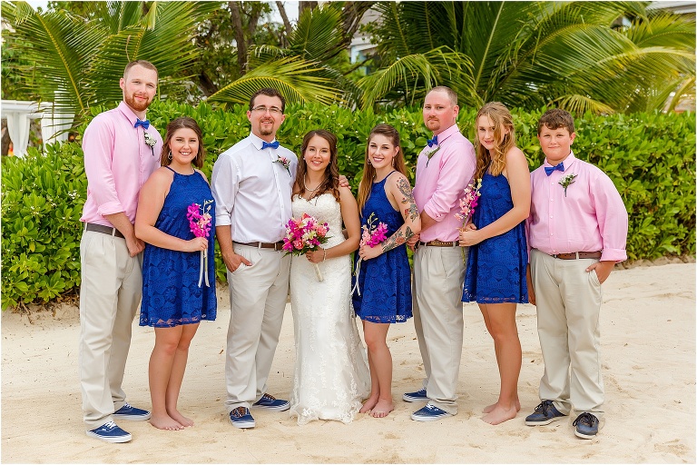 the wedding party smiles together on the beach in their pink and navy blue color scheme