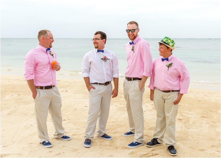 the groom and his groomsmen laugh together on the beach