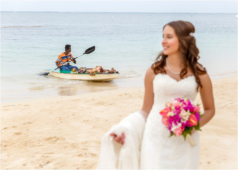 a local man rows his boat up onto the beach to sell his goods right behind the bride