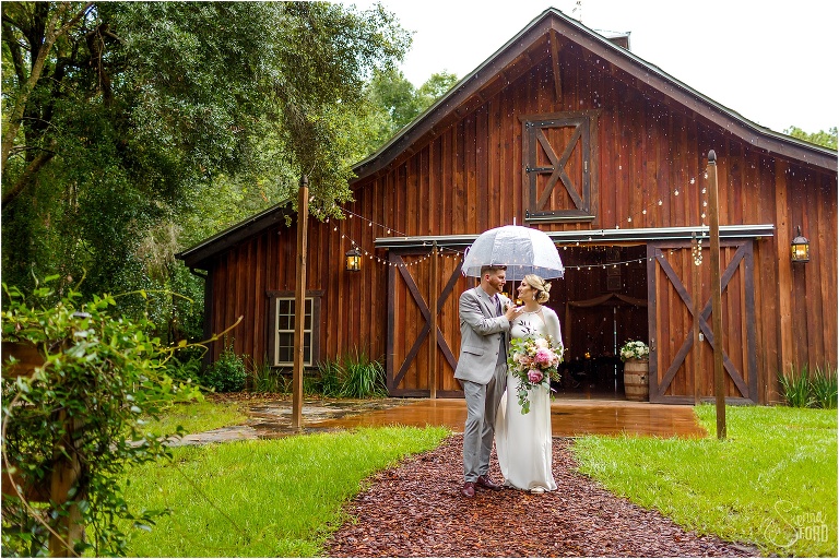bride & groom stroll under umbrella at Florida barn wedding
