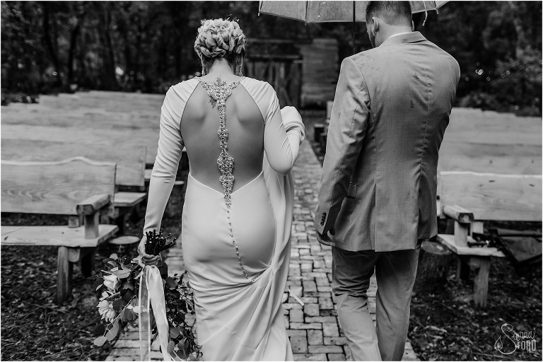 groom leads bride down brick path under umbrella at Florida barn wedding