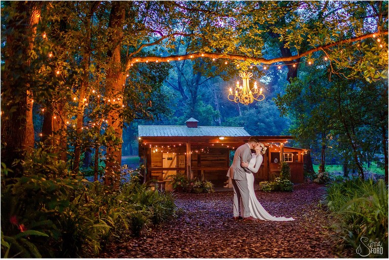 groom kisses bride under chandelier at dusk at DeLand barn wedding