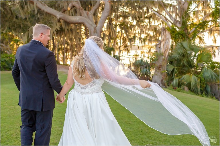 wind catches bride's veil as bride & groom walk hand in hand along Little Lake Harris