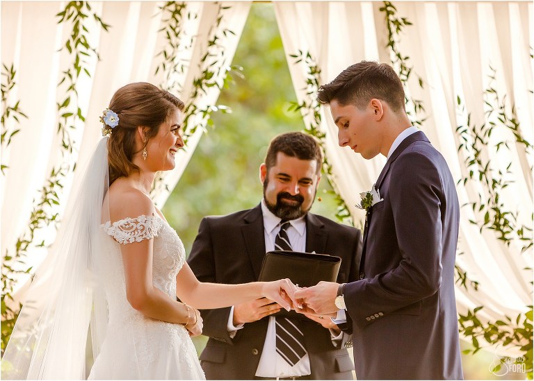 bride grins as groom places ring on her finger during Club Lake Plantation wedding ceremony