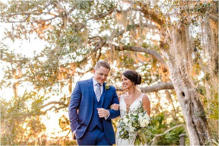 bride & groom walk arm in arm through trees at Amelia Island wedding