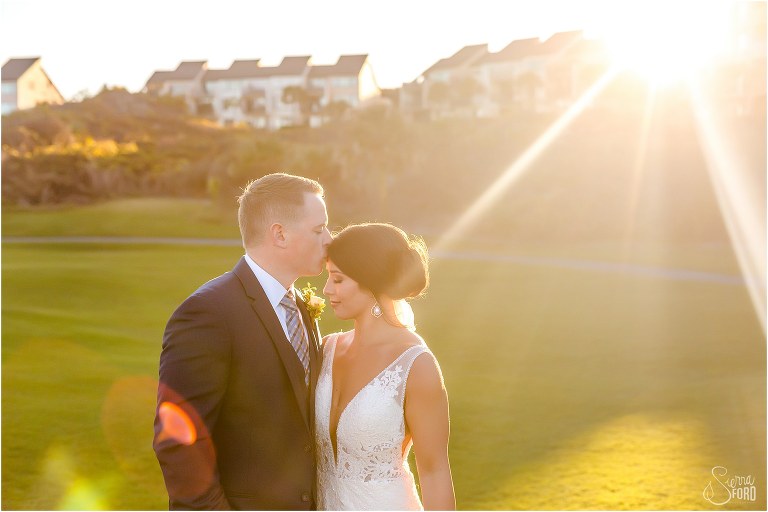 groom kisses bride on forehead as sun flares behind them at Amelia Island wedding