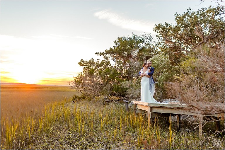 groom holds bride on wooden landing as the sun sets behind them at Amelia Island wedding
