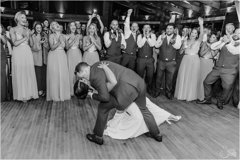 wedding party cheers behind couple as groom dip kisses bride during first dance at Amelia Island wedding reception