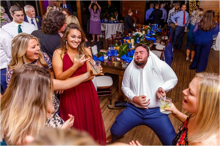 guests laugh as groomsmen dances with shirt over his head at Amelia Island wedding reception