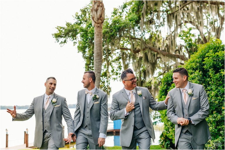 groom & his groomsmen joke around by the water in grey suits before Town Manor wedding